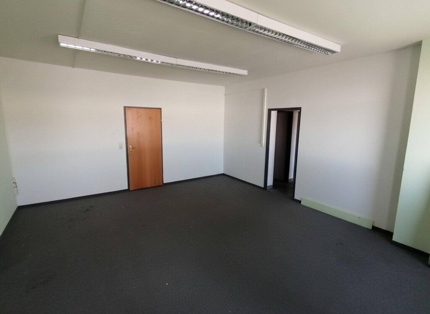 Leeres Büro mit Teppichboden und mehreren Türen, bereit zur Einrichtung.