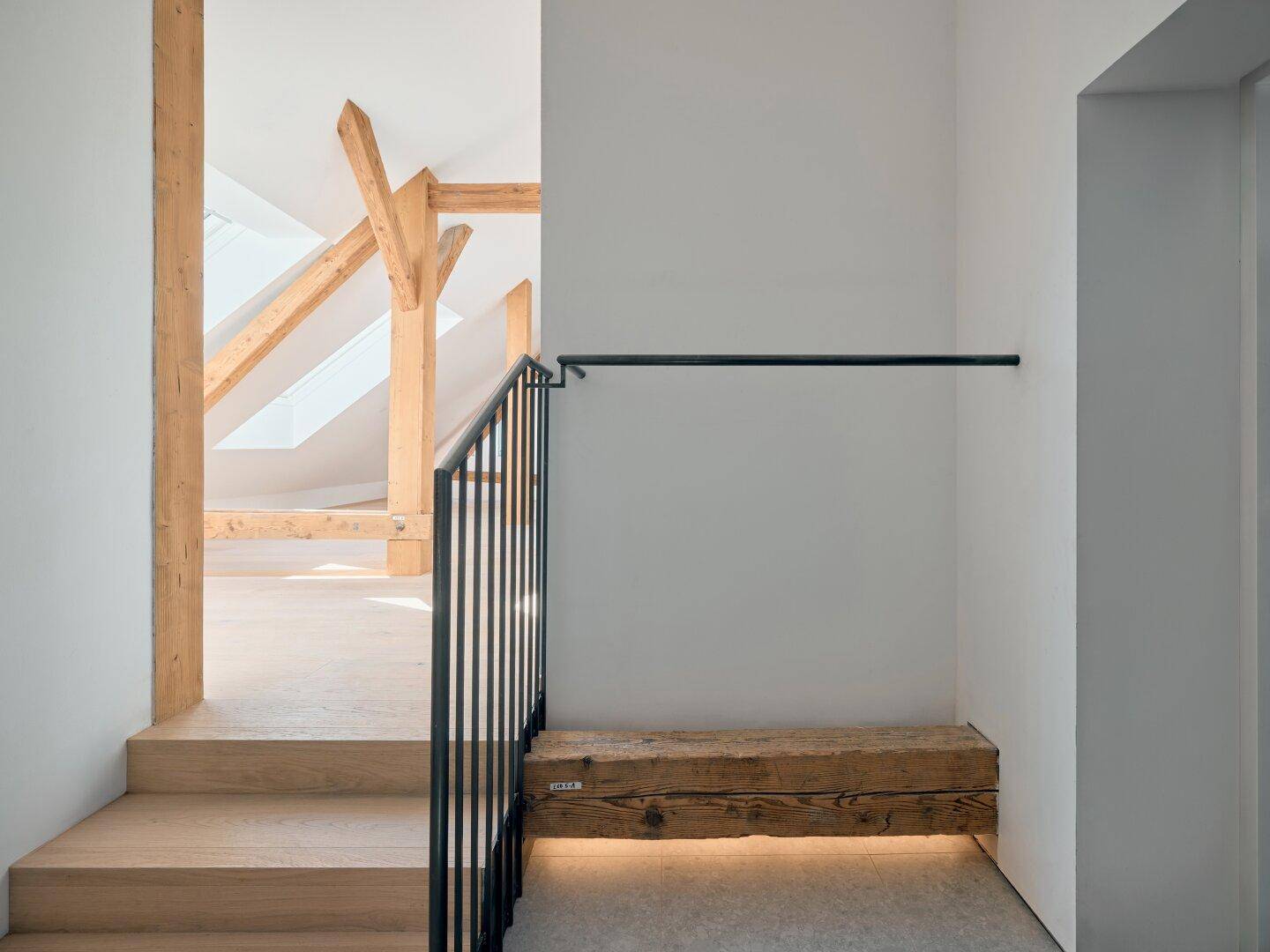 Heller Flur mit Holztreppe, schwarzem Geländer und einer rustikalen Holzbank mit Beleuchtung.
