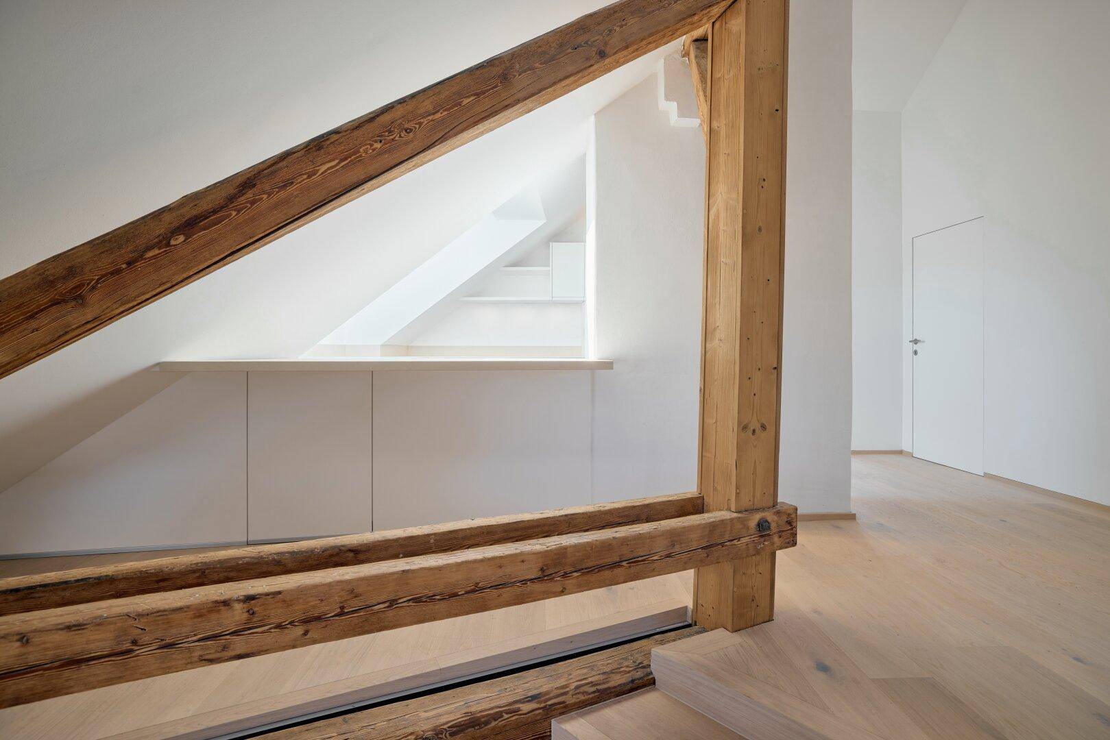 Dachbodenbereich mit integrierten weißen Schränken, Holzbalken und hellem Holzboden.