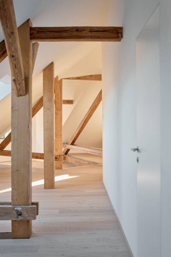 Langer Dachbodenflur mit freiliegenden Holzbalken, hellem Boden und weiß gestrichenen Wänden.