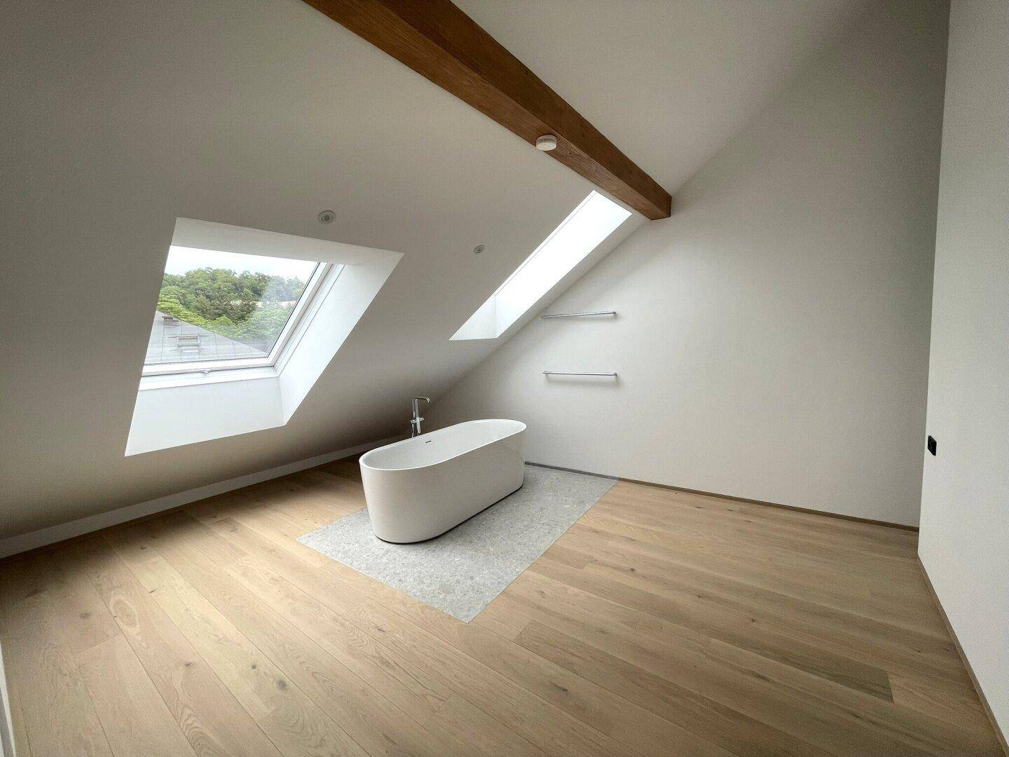 Geräumiges Badezimmer im Dachgeschoss mit freistehender Badewanne, Holzboden und Dachfenstern.