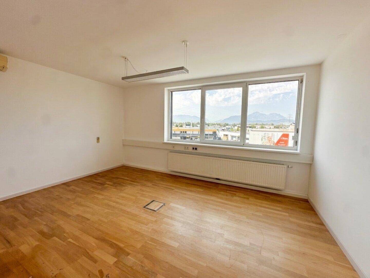 Heller Büroraum mit Holzboden, großen Fenstern und Panoramablick auf die Stadt und Berge.