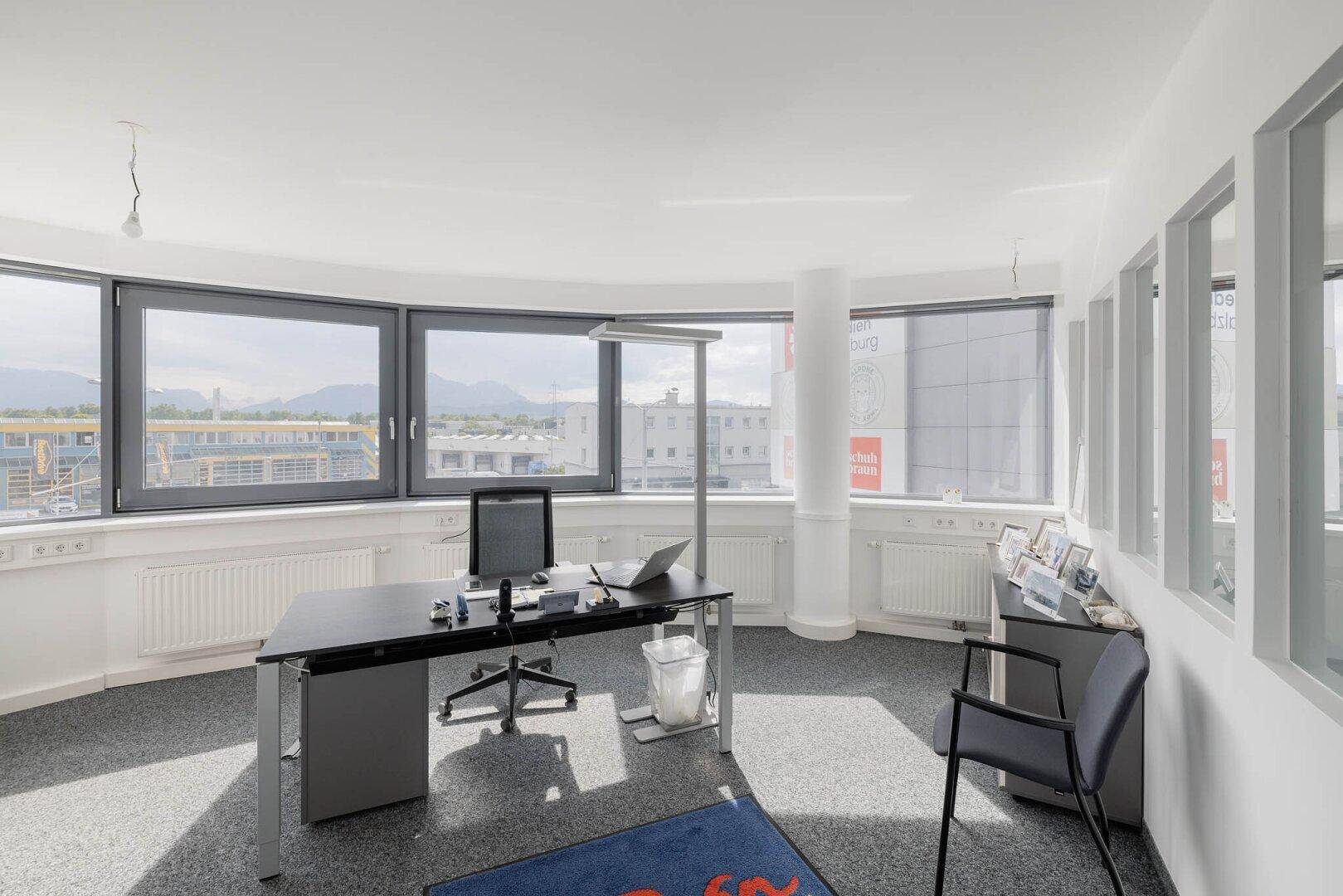Modern eingerichtetes Büro mit Schreibtisch, Bürostuhl und großen Fenstern mit Panoramablick.