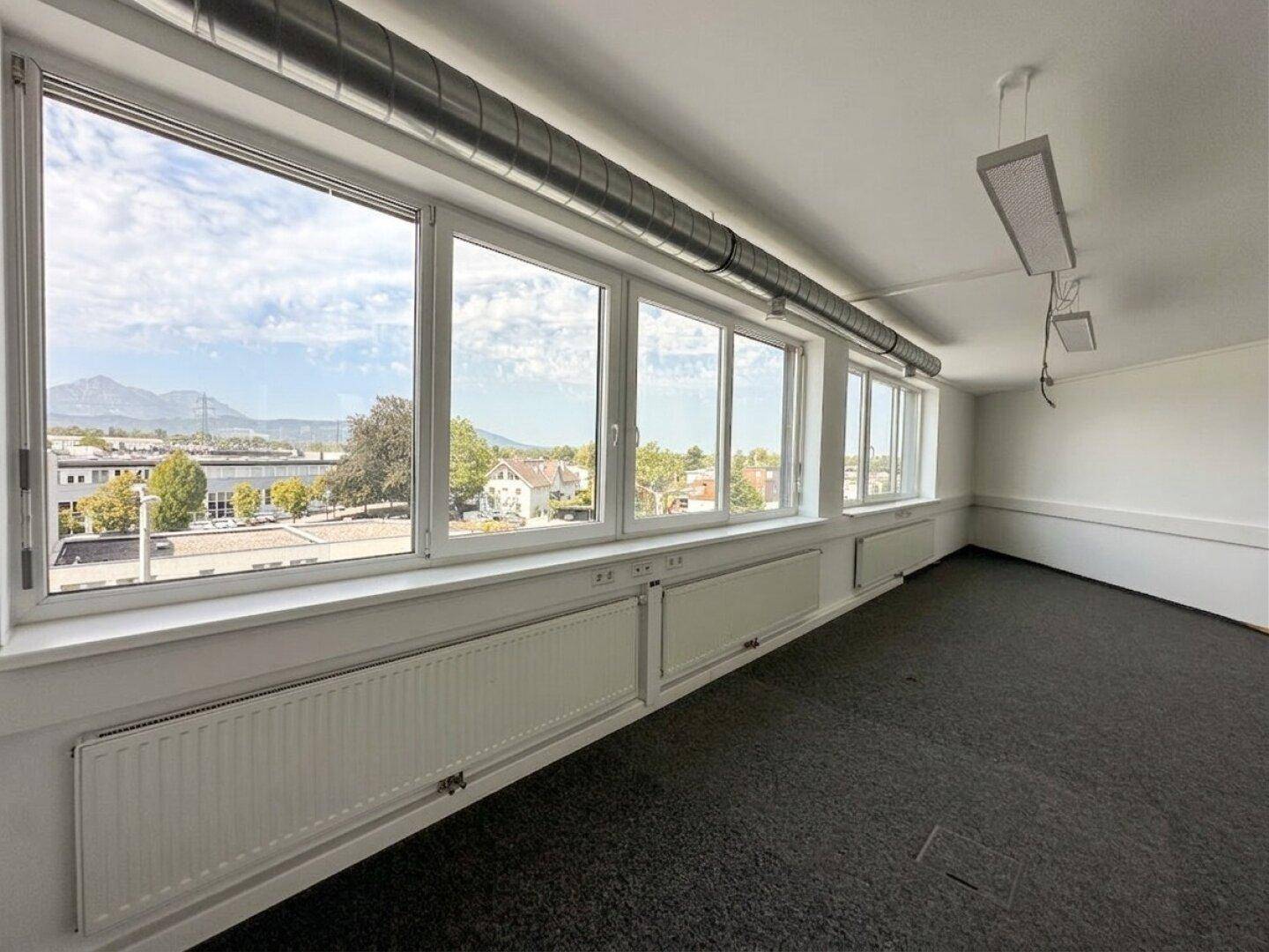 Helles Büro mit einer Fensterfront, die einen weiten Blick auf die Umgebung und Berge bietet.