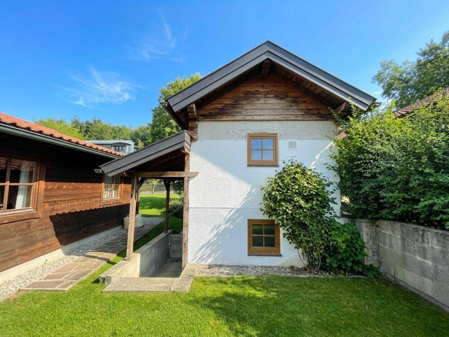 Seitenansicht eines Hauses mit weißer Fassade, Holzelementen und einem kleinen grünen Gartenbereich.