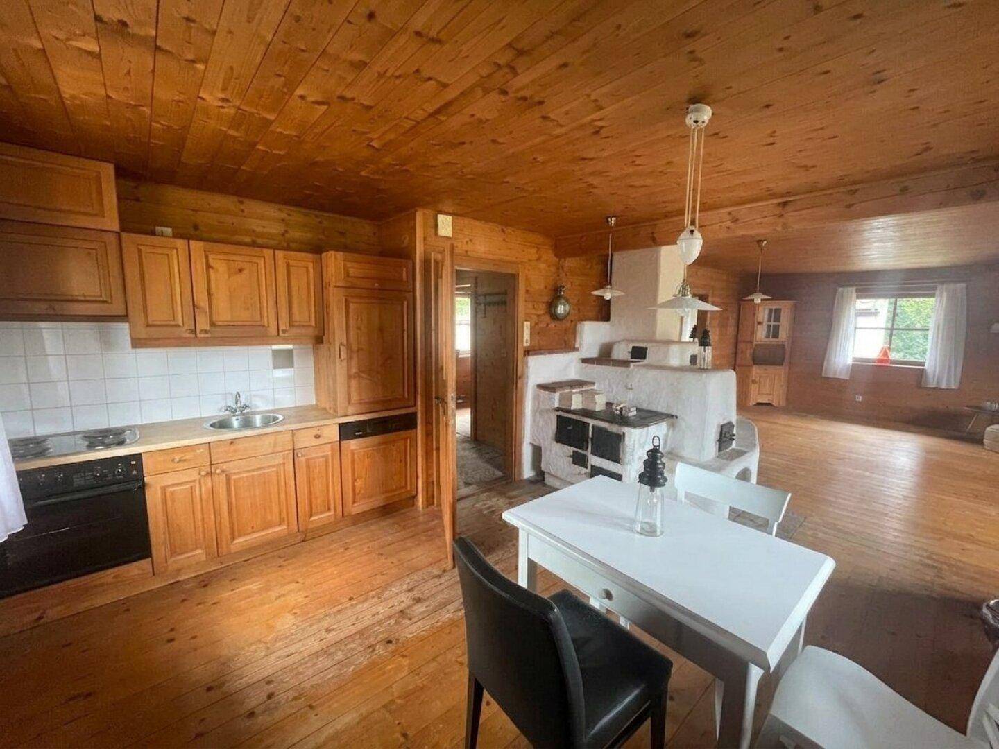Gemütlicher Wohn-Essbereich mit Holzböden, Holzvertäfelung und einem traditionellen Kachelofen.