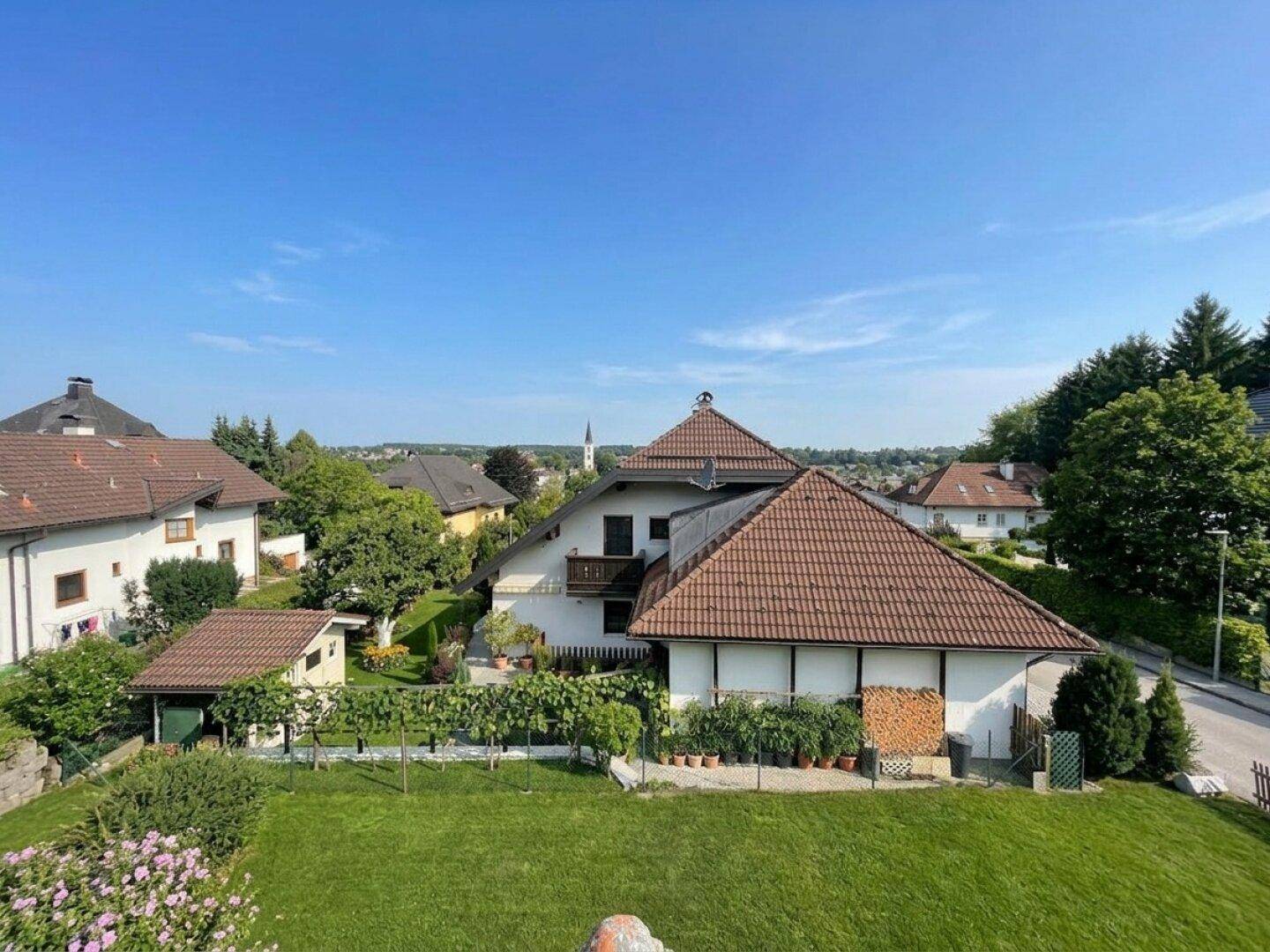 Weitläufiger Gartenbereich mit Rasen, Weinreben und Blick auf die umliegenden Häuser und Landschaft.