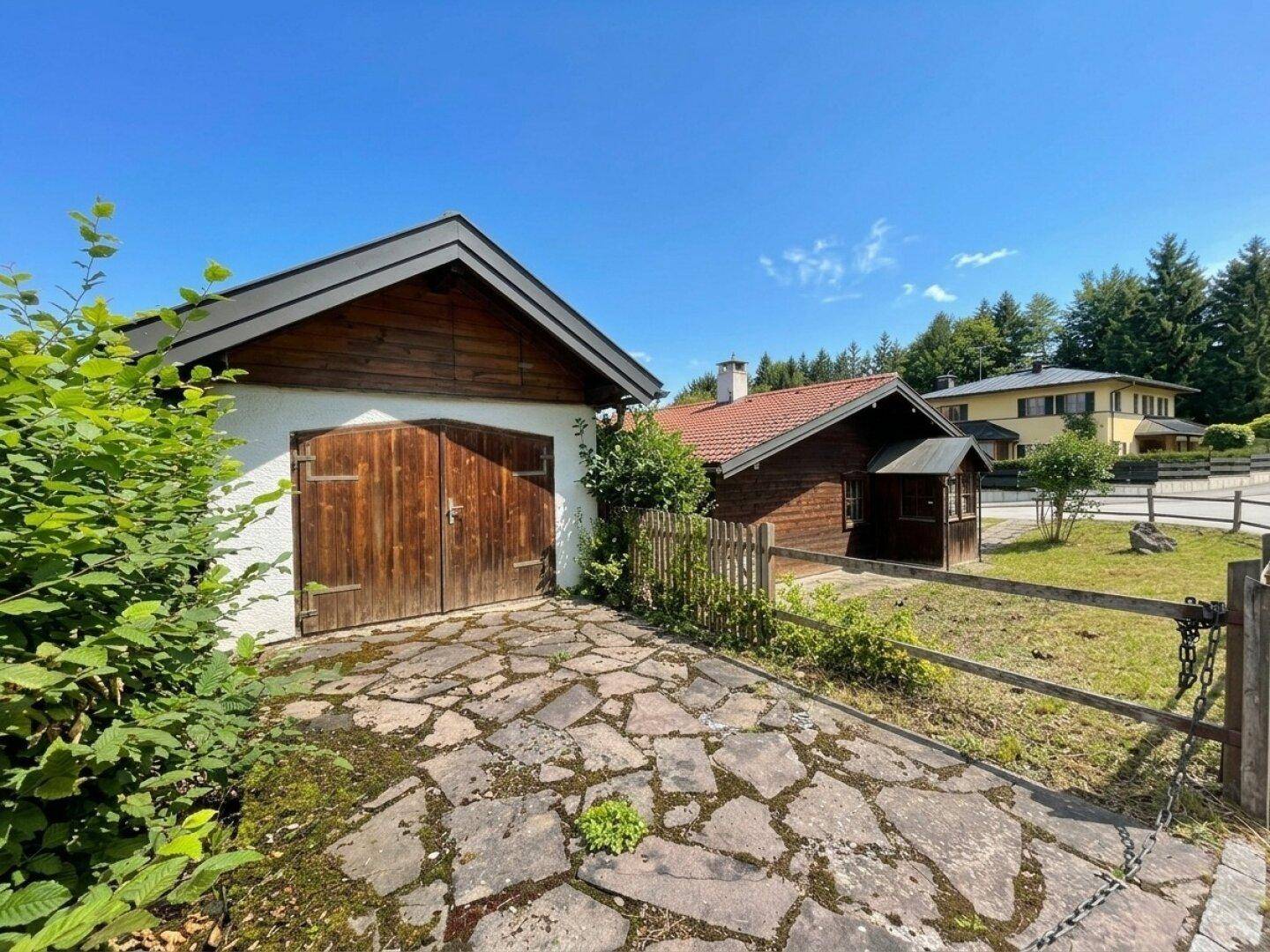 Rustikale Holzgarage mit gepflasterter Auffahrt und Holzzaun in ländlicher Umgebung.