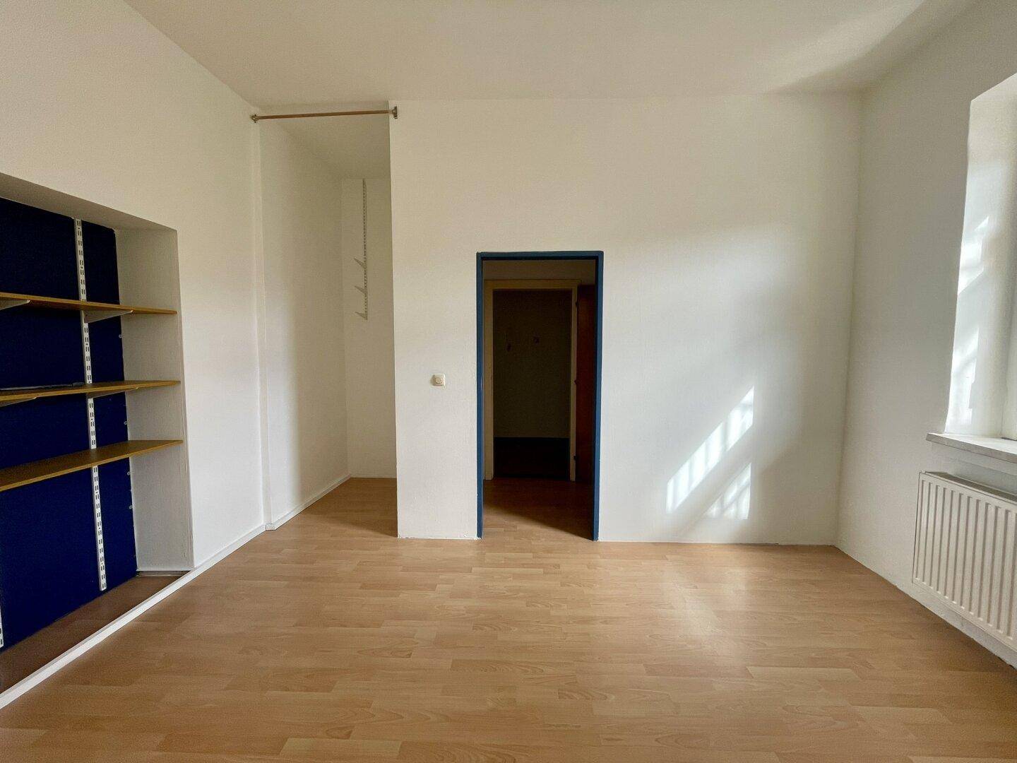 Leerer Raum mit Holzboden und blauen Einbauregalen, bietet vielseitige Nutzungsmöglichkeiten.