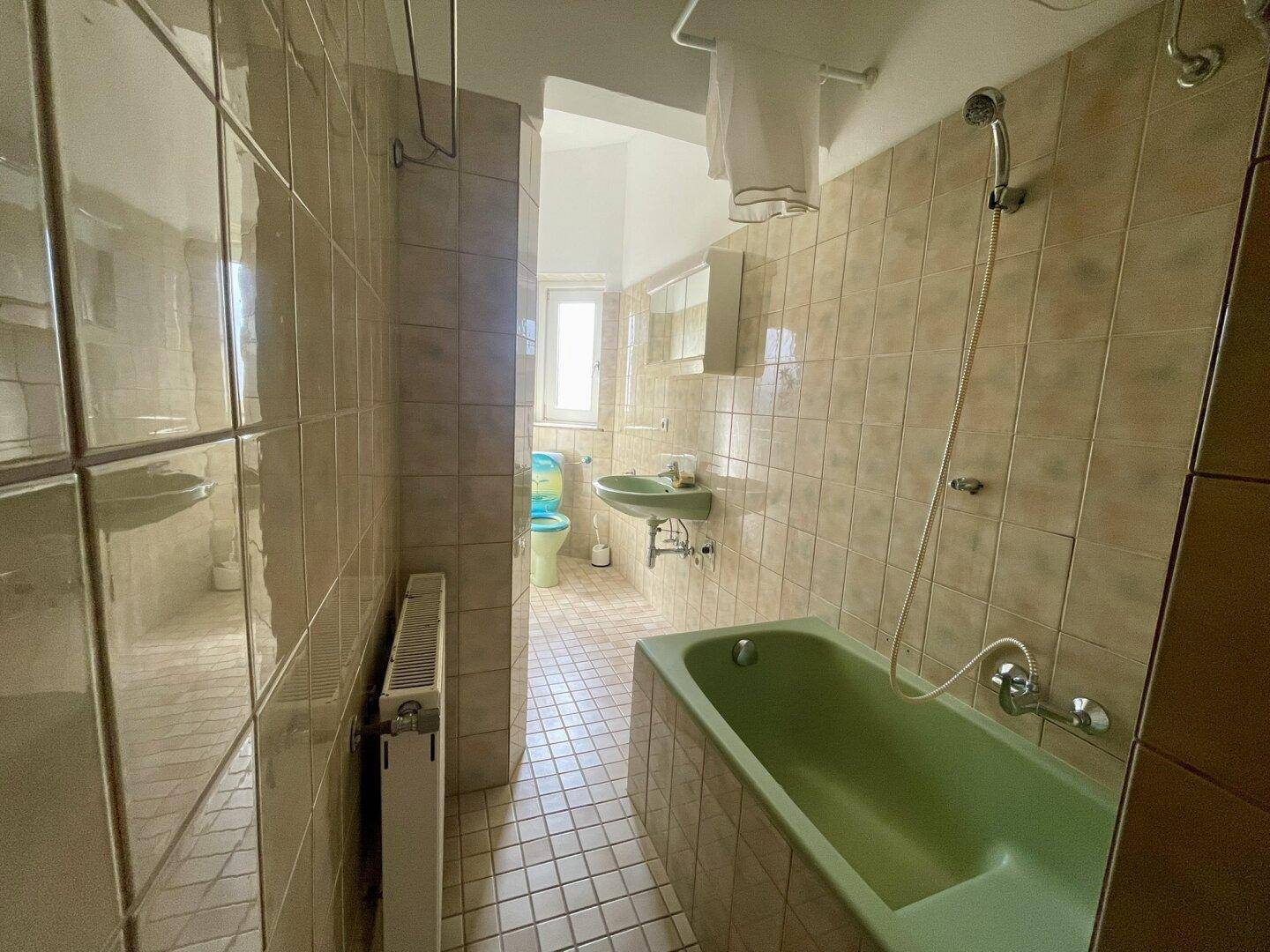 Badezimmer im Stil der 80er Jahre mit grüner Badewanne, Waschbecken und beigefarbenen Fliesen.