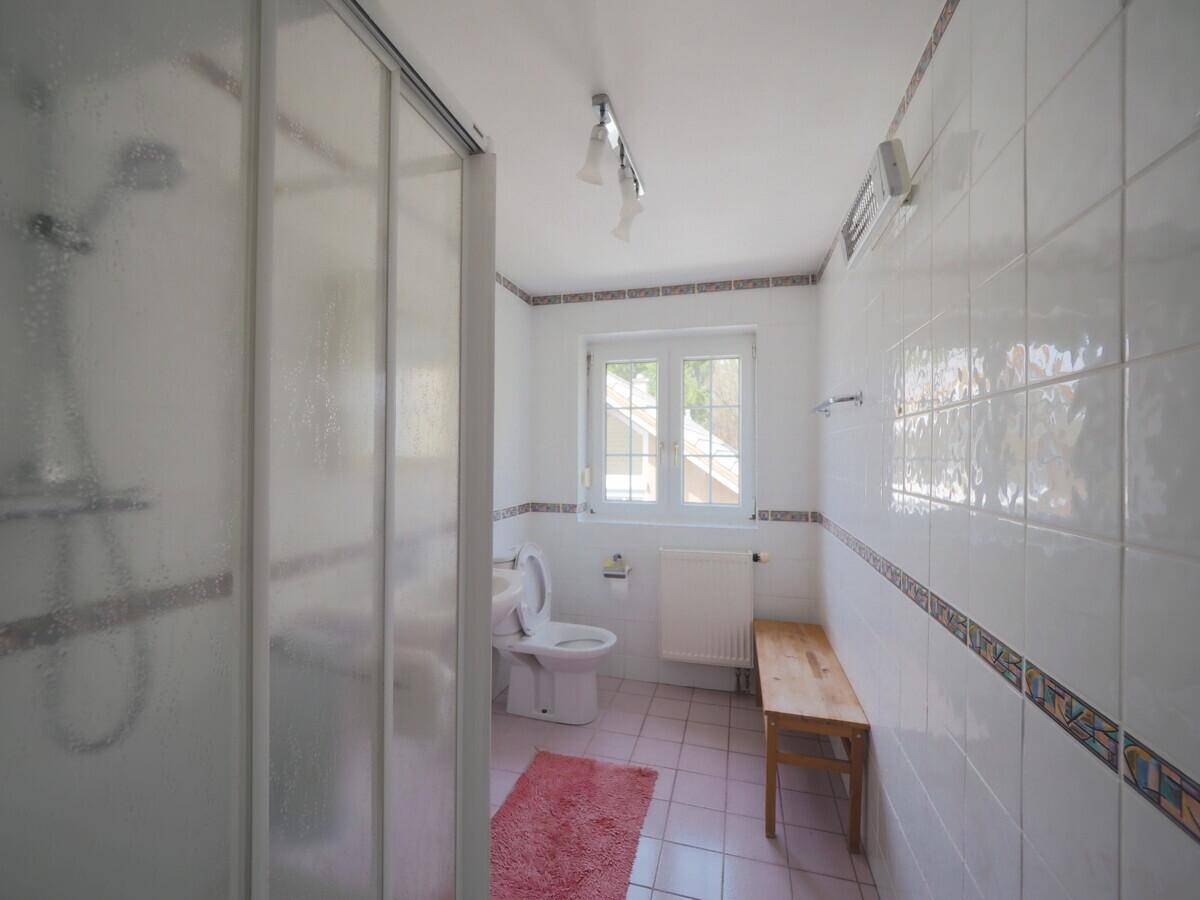Badezimmer mit Dusche, WC und Fenster, ausgestattet mit hellen Fliesen.