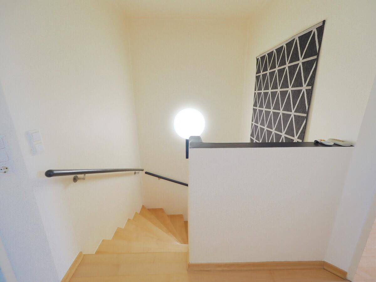 Treppenaufgang mit Holzstufen, modernem Geländer und runder Wandleuchte.