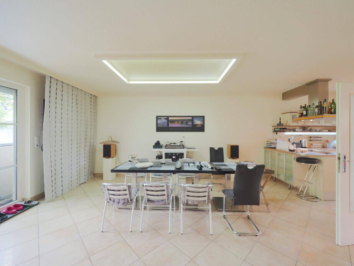 Offener Wohn- und Essbereich mit moderner Deckenbeleuchtung und Zugang zum Balkon.