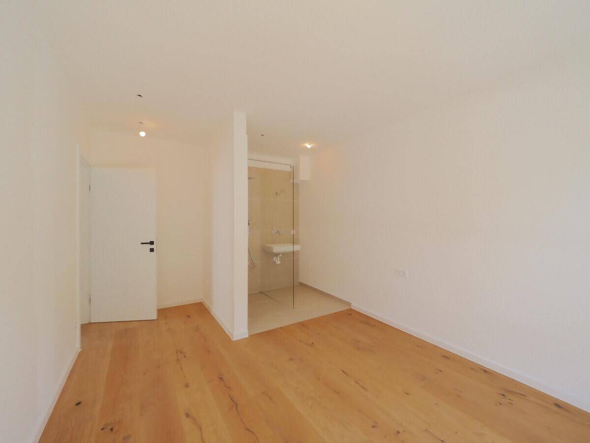 Modernes Zimmer mit Holzboden und integriertem Duschbereich mit Glasabtrennung und Waschbecken.