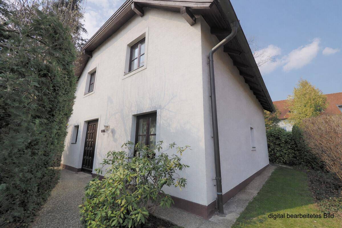 Seitenansicht des Hauses mit weißer Fassade, braunen Fenstern und gepflegter Umgebung.