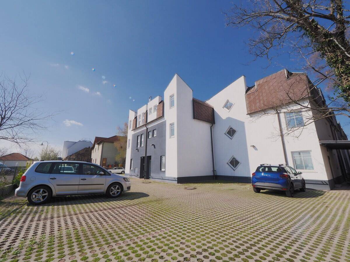 Ansicht des modernen Wohngebäudes von der Seite mit Parkplätzen unter blauem Himmel.