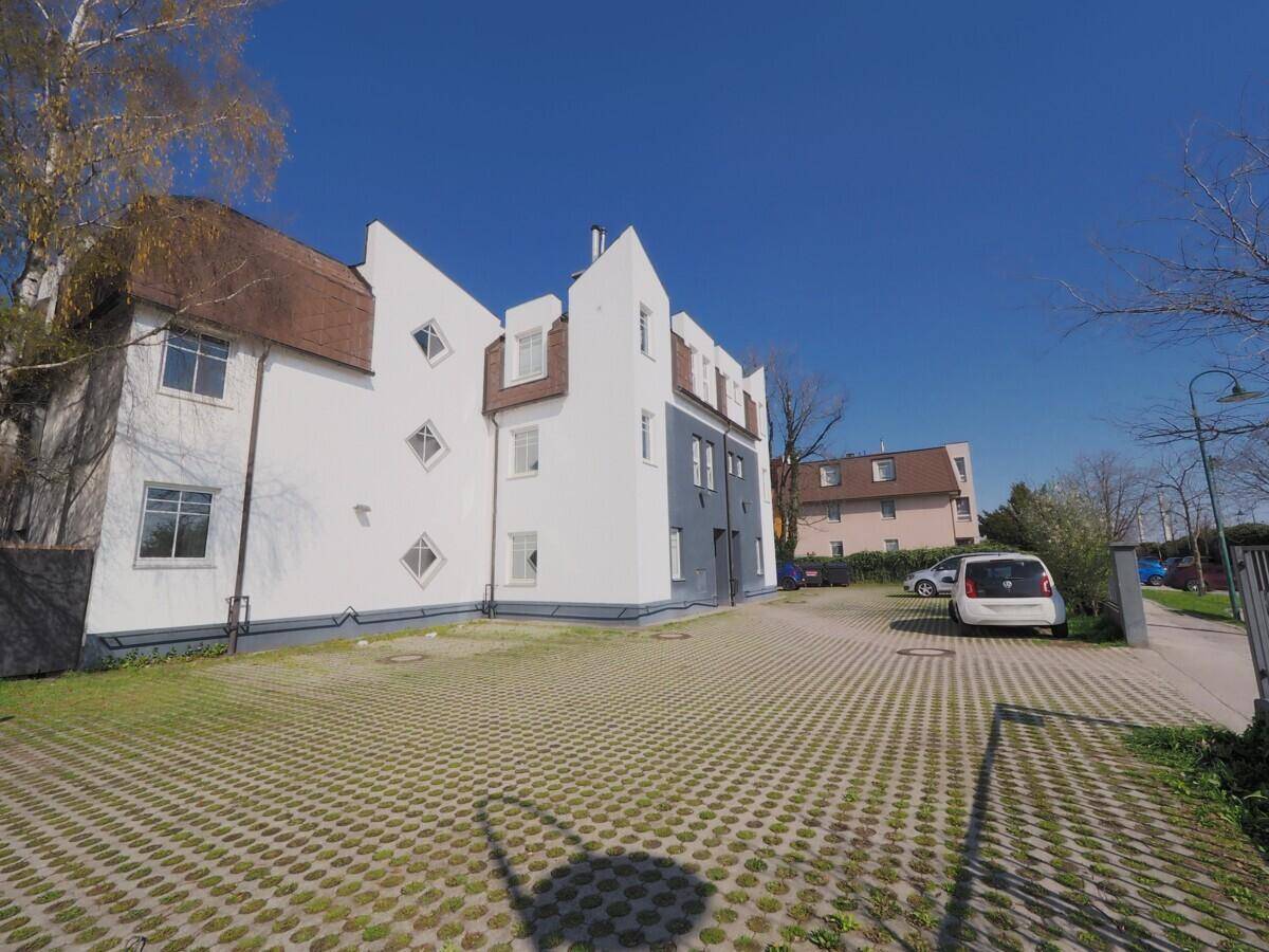 Seitenansicht des modernen Gebäudes mit weißer und grauer Fassade sowie Parkflächen.