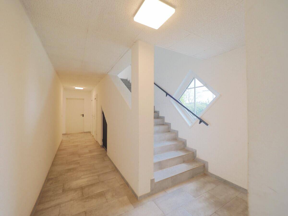 Heller Flur mit Treppenaufgang und einem markanten rautenförmigen Fenster.