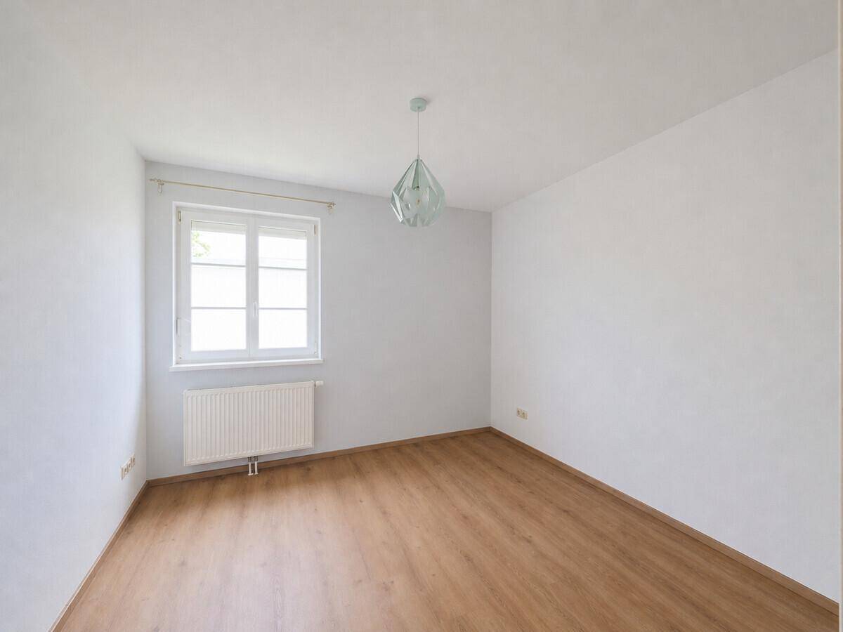 Leeres Zimmer mit Fenster, Laminatboden und schlichter Deckenleuchte.