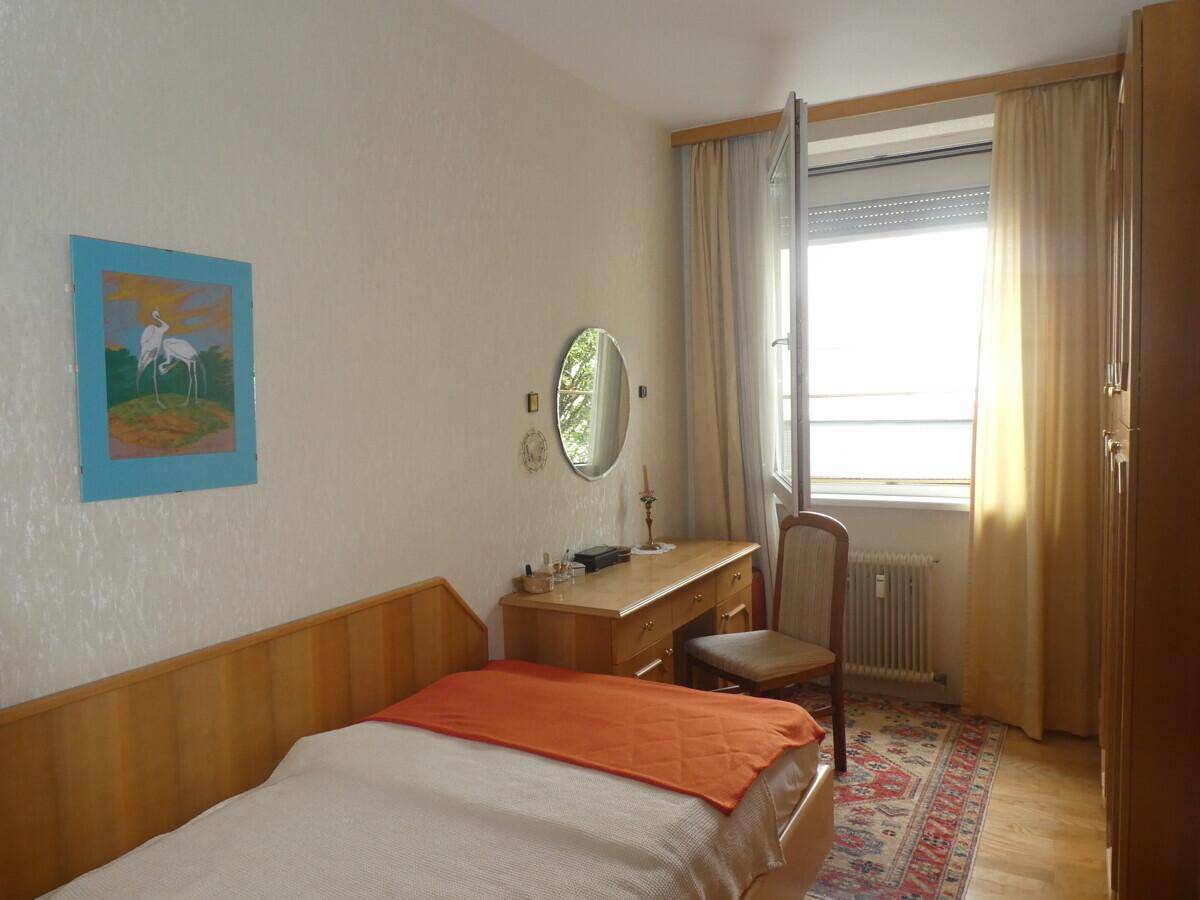 Helles Schlafzimmer mit Einzelbett, Schreibtisch und Fenster mit Blick nach draußen.