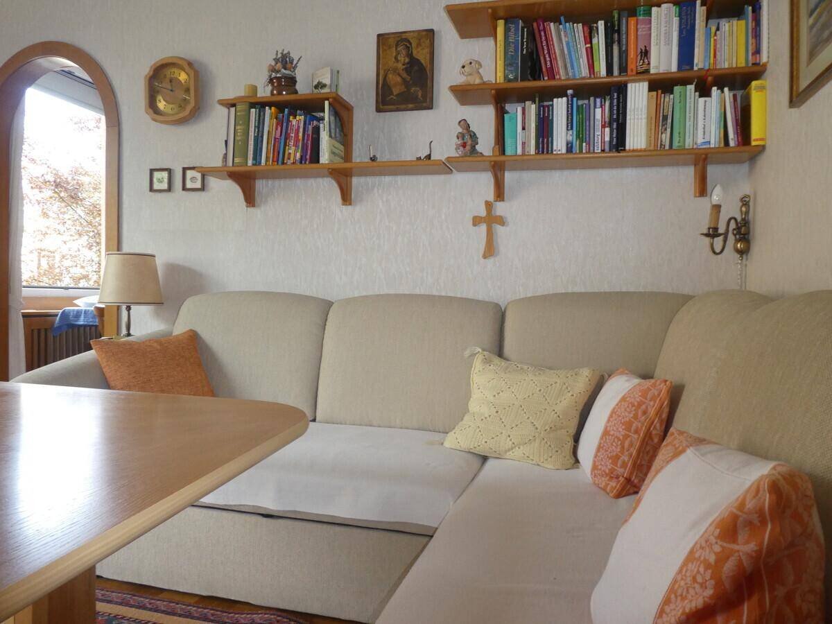 Gemütlicher Wohnbereich mit beigem Ecksofa, Holztisch und Bücherregalen an der Wand.