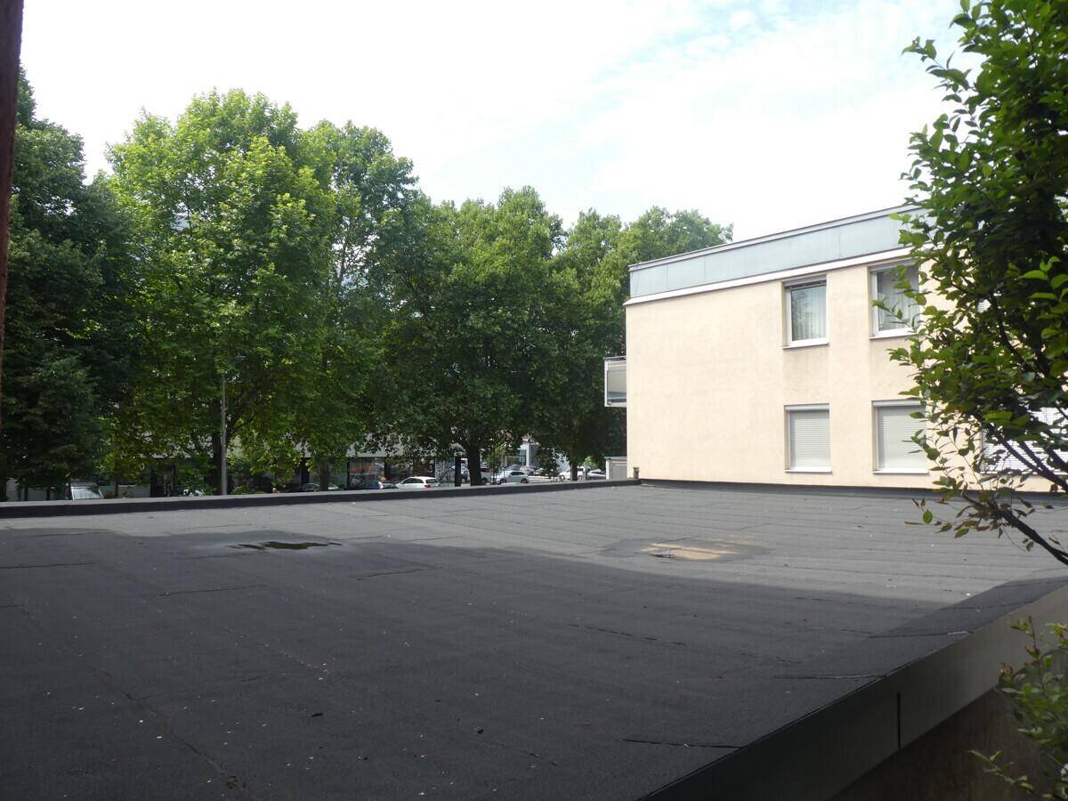 Flachdach eines Gebäudes mit Blick auf umliegende Bäume und weitere Gebäude.