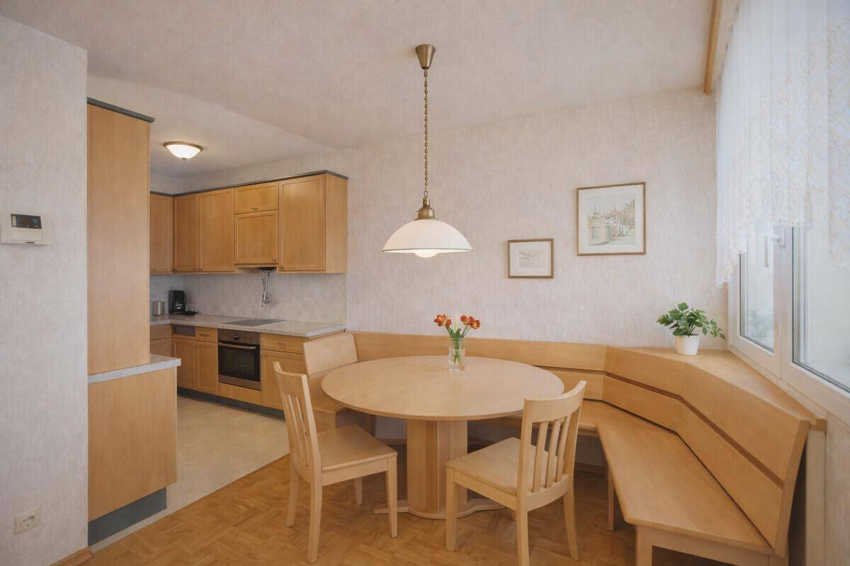 Helle Küche mit Holzeinbauten, integriertem Essbereich und Fenster für natürliches Licht.