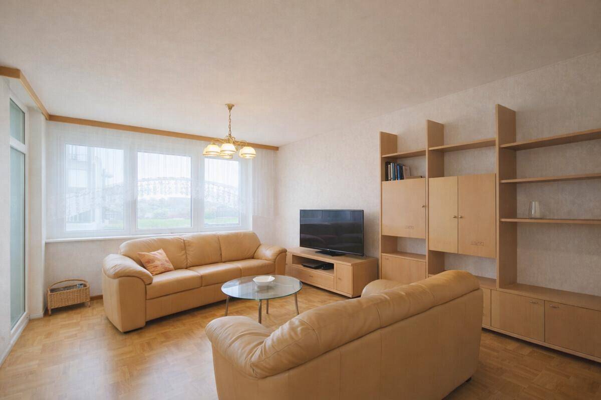 Gemütliches Wohnzimmer mit beigen Ledersofas, Holzboden und großen Fenstern für viel Tageslicht.