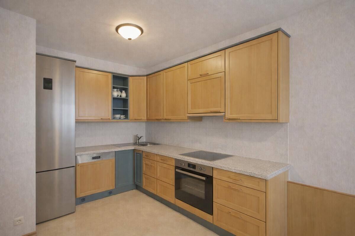 Funktionale Küche mit hellen Holzschränken, modernen Geräten und einem großen Kühlschrank.