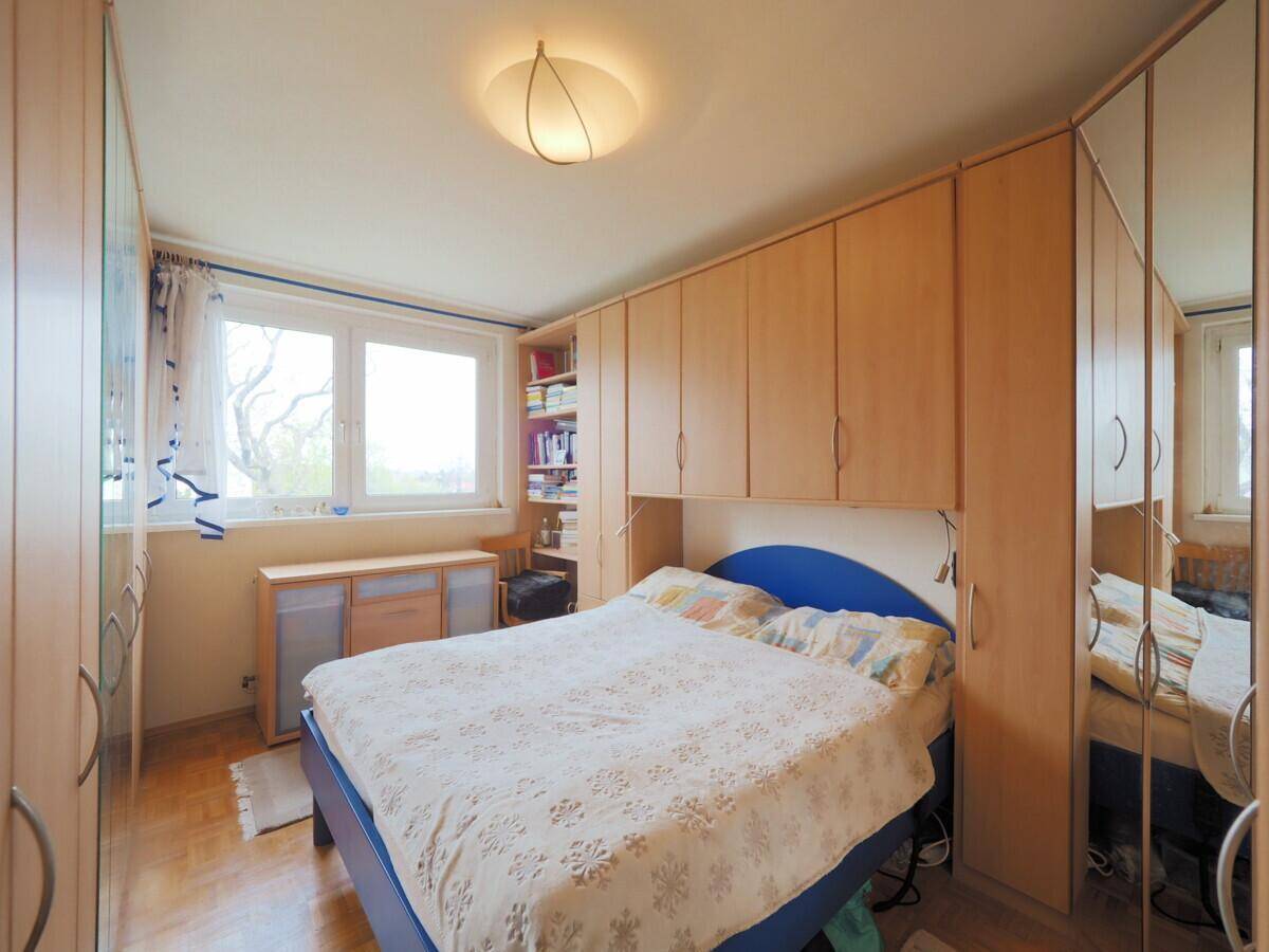 Schlafzimmer mit Doppelbett, Einbauschränken und Fenster, das viel Tageslicht hereinlässt.