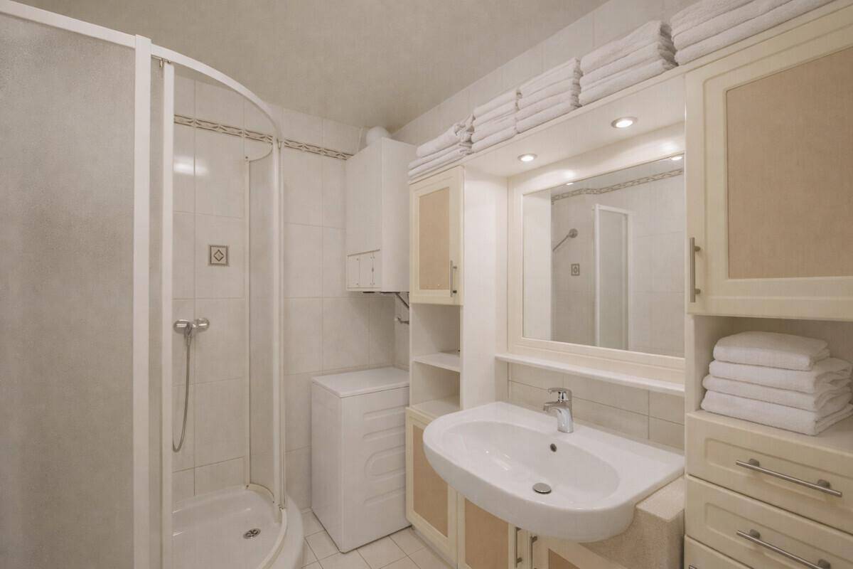 Modernes Badezimmer mit Duschkabine, Waschbecken und Spiegelschrank, in hellen Fliesen gehalten.