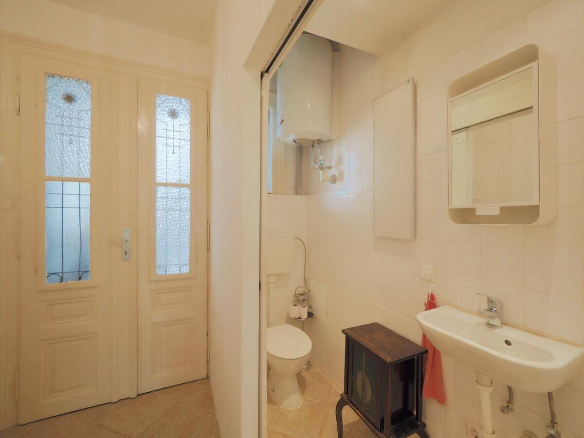 Separates WC mit Toilette, Waschbecken und dekorativen Doppeltüren, hell gefliest.