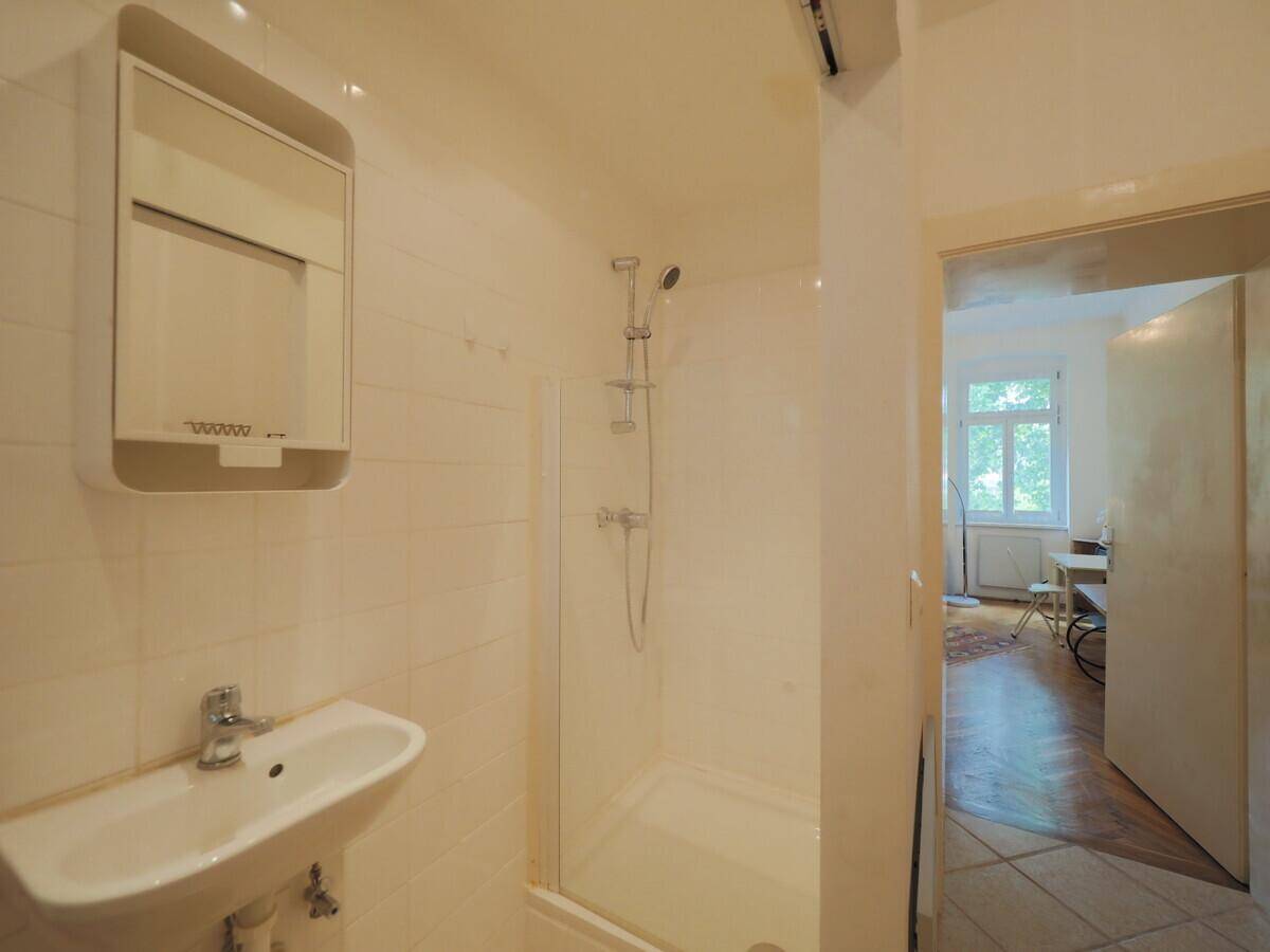 Kleines Badezimmer mit Duschkabine, Waschbecken und Spiegelschrank, hell gefliest.