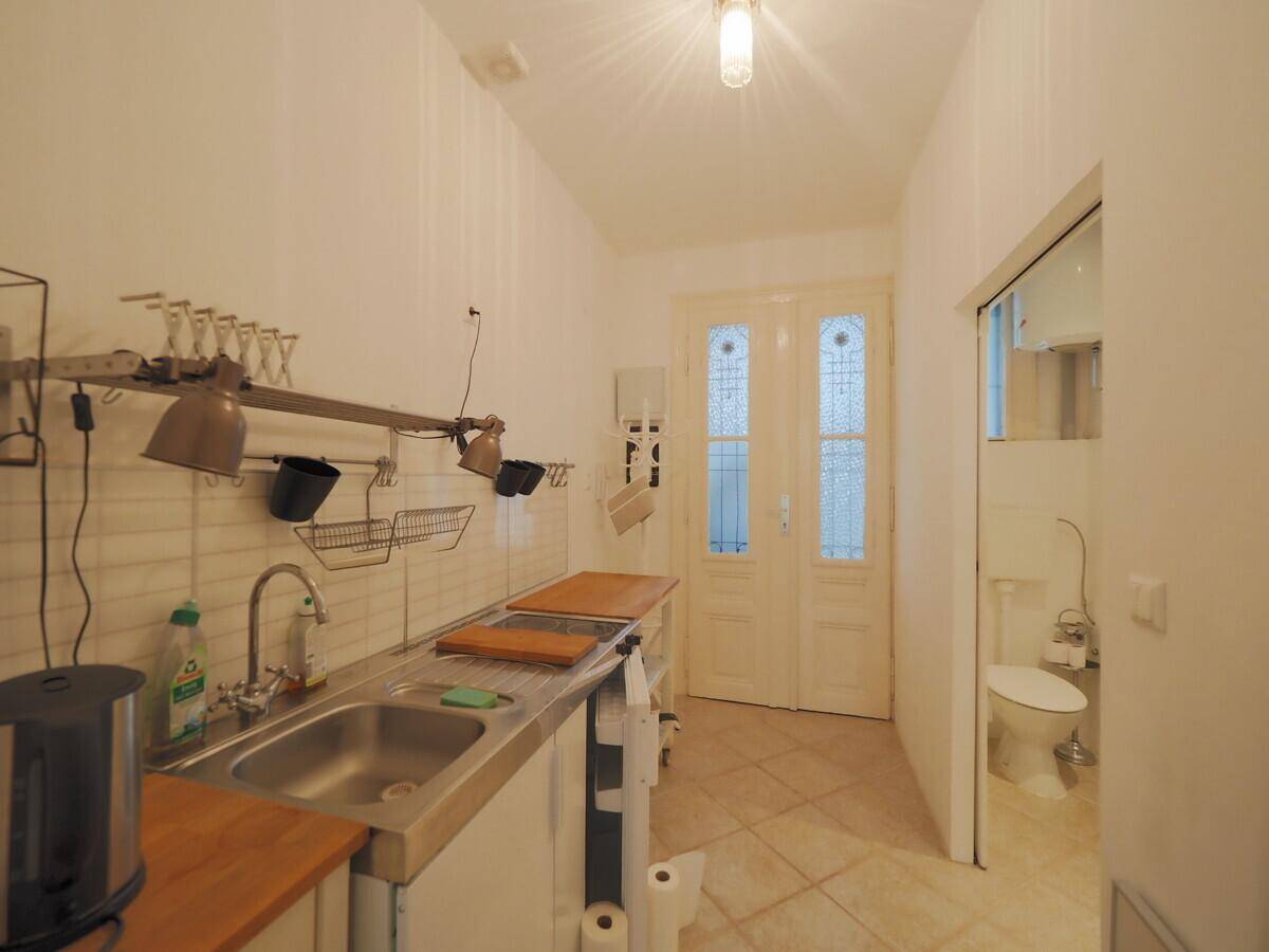 Schmale Küche mit Spülbecken, Kochfeld und Zugang zu einem separaten WC.