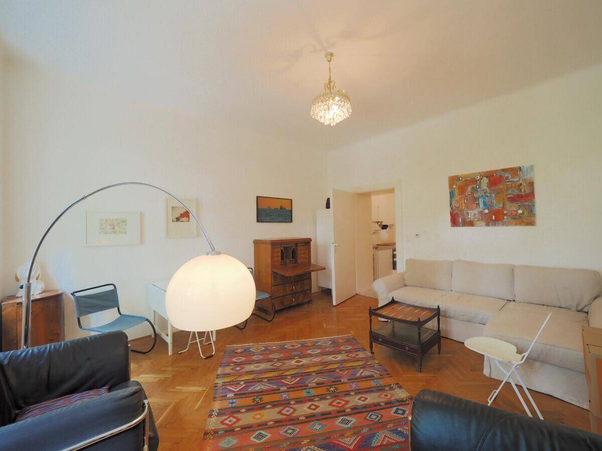 Geräumiges Wohnzimmer mit Parkettboden, Sofa und einem dekorativen Teppich, der zum Entspannen einlädt.