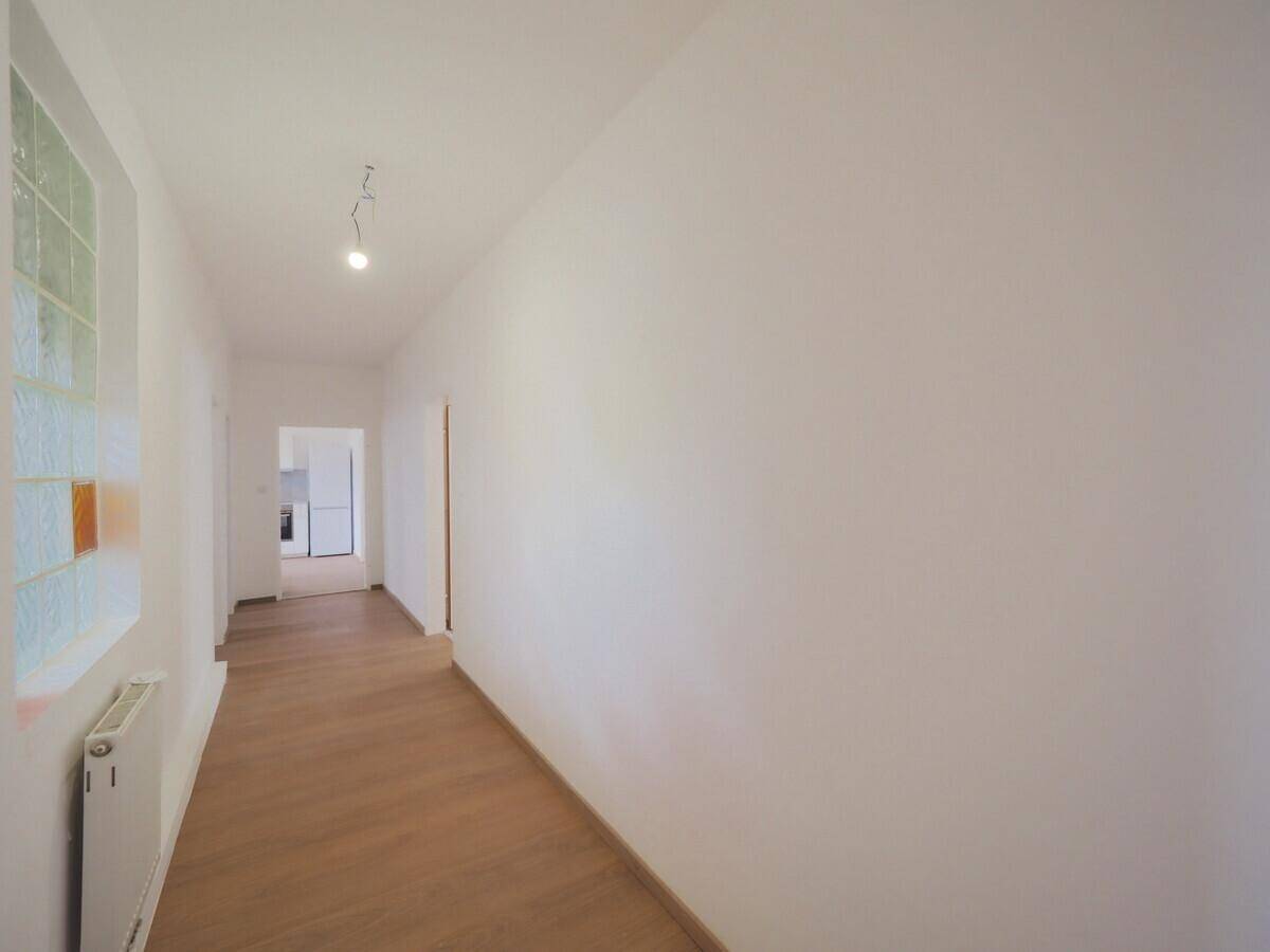 Langer, heller Flur mit Laminatboden, weißen Wänden und einem Fenster mit Strukturglas.