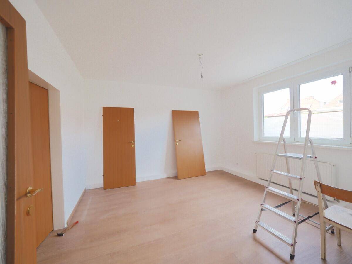 Geräumiges Zimmer mit Laminatboden, weißen Wänden und einem Fenster, bereit für die Renovierung.