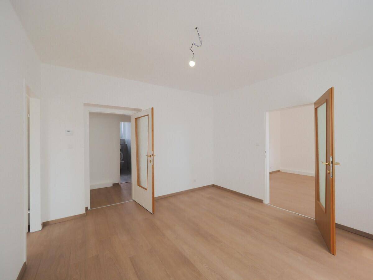 Heller Raum mit Laminatboden und weißen Wänden, durch zwei Türen mit Glaseinsätzen verbunden.
