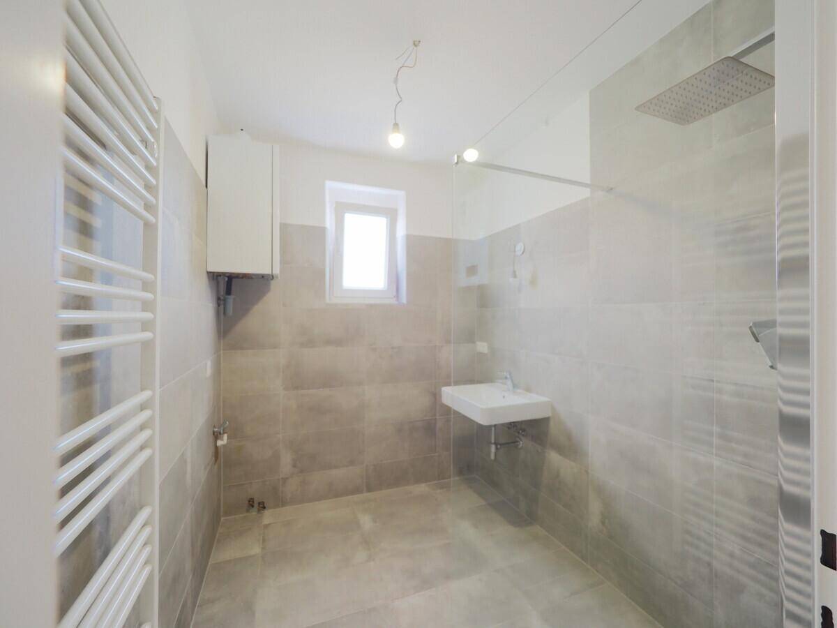 Modernes Badezimmer mit grauen Fliesen, begehbarer Dusche, Regendusche und beheiztem Handtuchhalter.