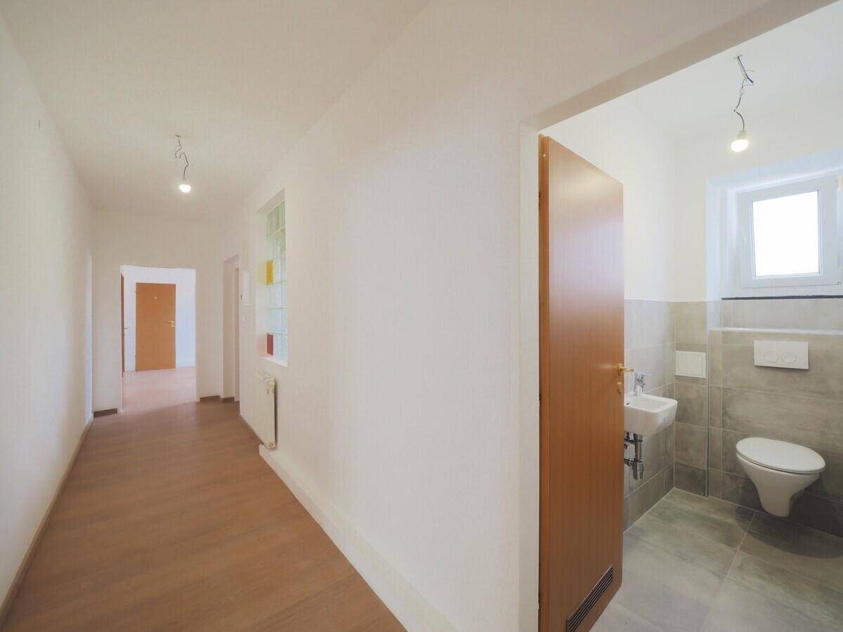 Heller Flur mit Laminatboden, der zu einem modernen Badezimmer mit WC und Fenster führt.
