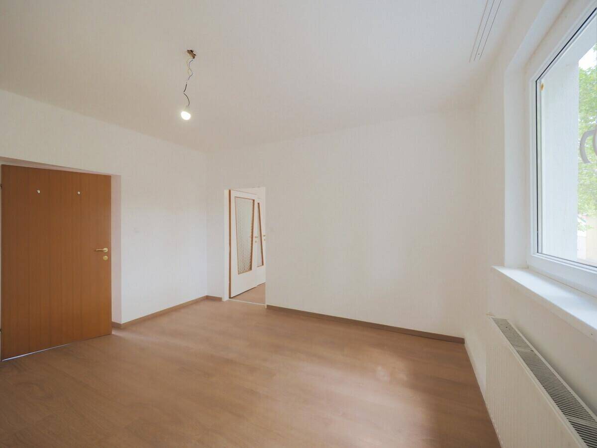 Helles Zimmer mit Laminatboden, weißen Wänden und einem großen Fenster, das viel Tageslicht hereinlässt.