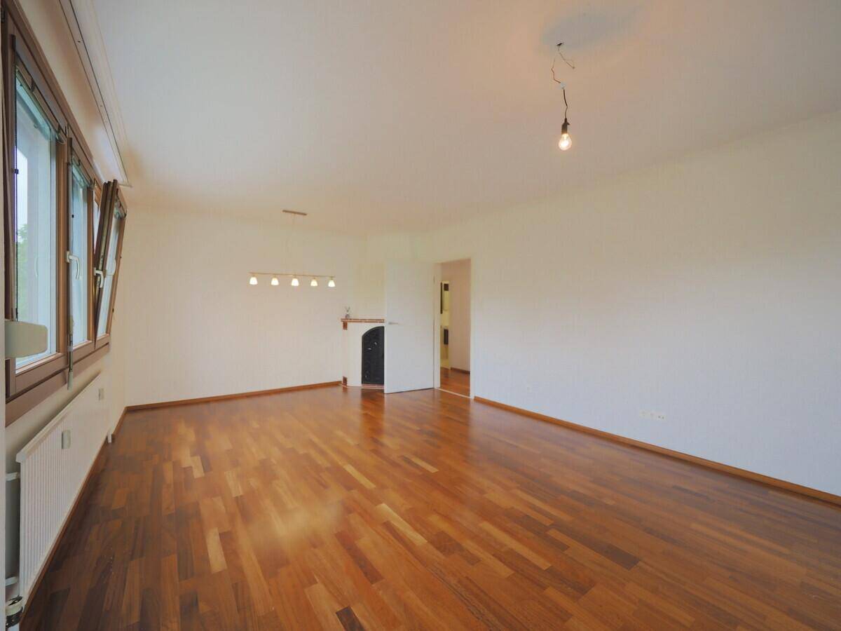 Geräumiges Wohnzimmer mit Holzboden und mehreren Fenstern, bereit zur individuellen Gestaltung.
