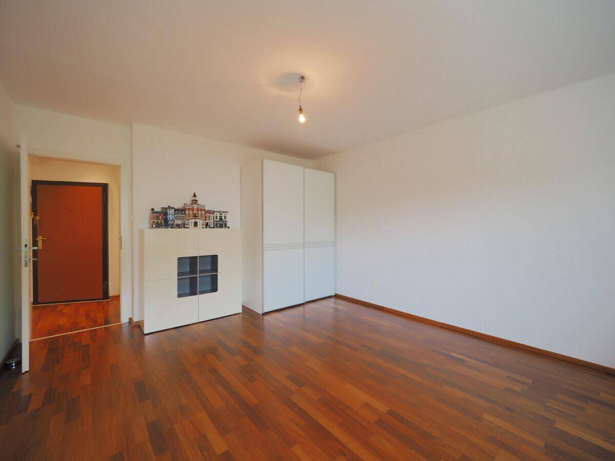 Heller Raum mit Holzboden, weißem Einbauschrank und Eingangstür, ideal als Schlafzimmer.