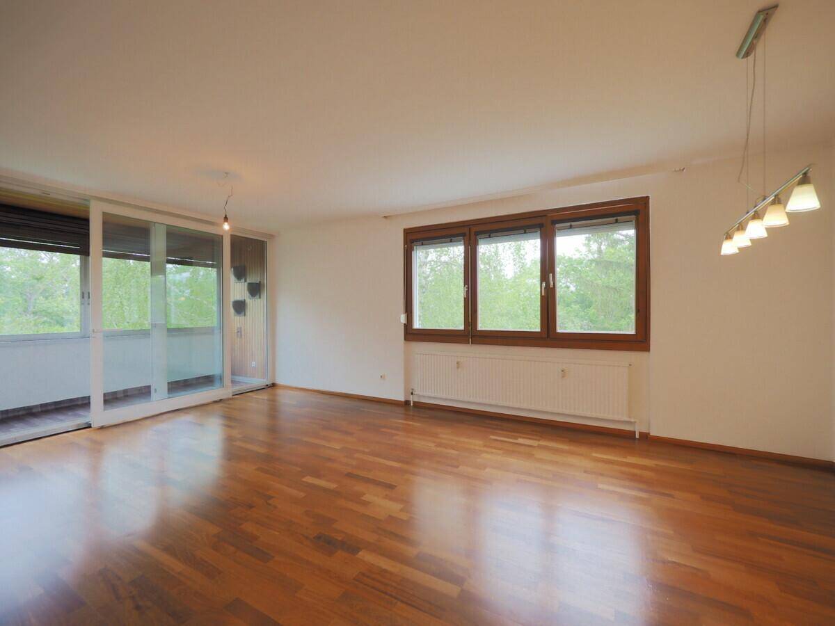 Helles Wohnzimmer mit Holzboden, großen Fenstern und Zugang zu einem überdachten Balkon.