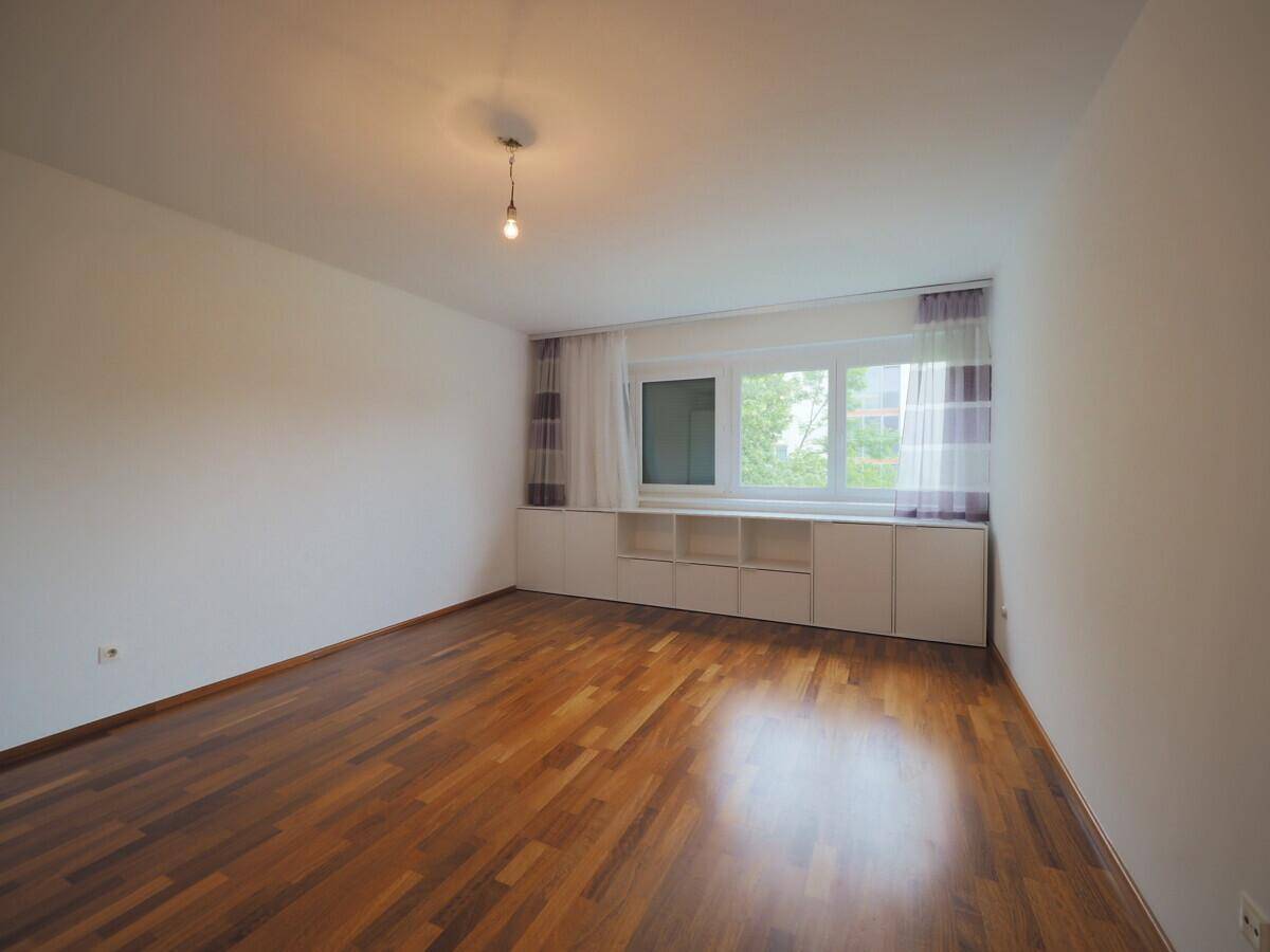 Schlafzimmer mit Holzboden, großem Fenster und integrierten Schränken unter der Fensterbank.