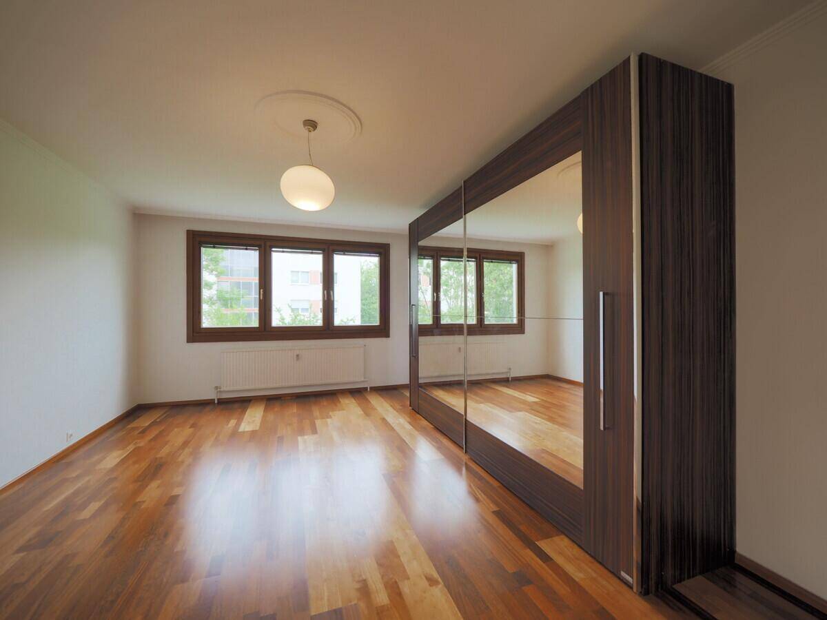Geräumiges Schlafzimmer mit Holzboden, Spiegelschrank und großen Fenstern mit Blick ins Grüne.