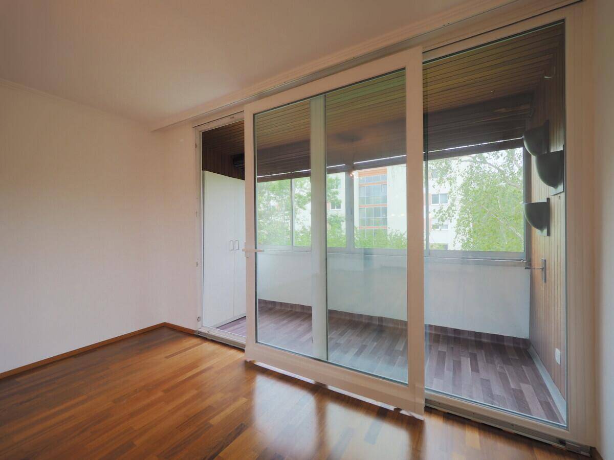 Heller Raum mit Holzboden und großen Schiebetüren, die zu einem Balkon führen.