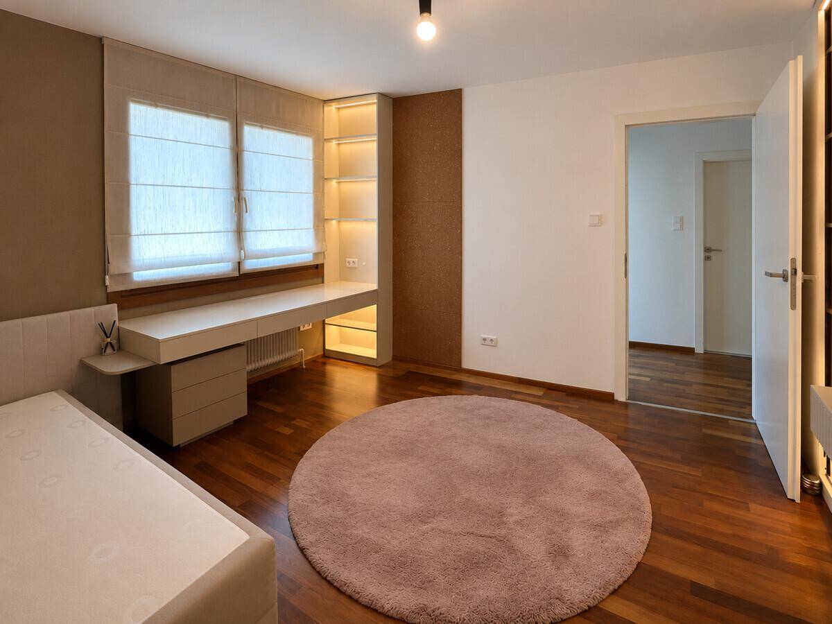 Helles Schlafzimmer mit Holzboden, integrierten Regalen und einem Schreibtisch am Fenster.