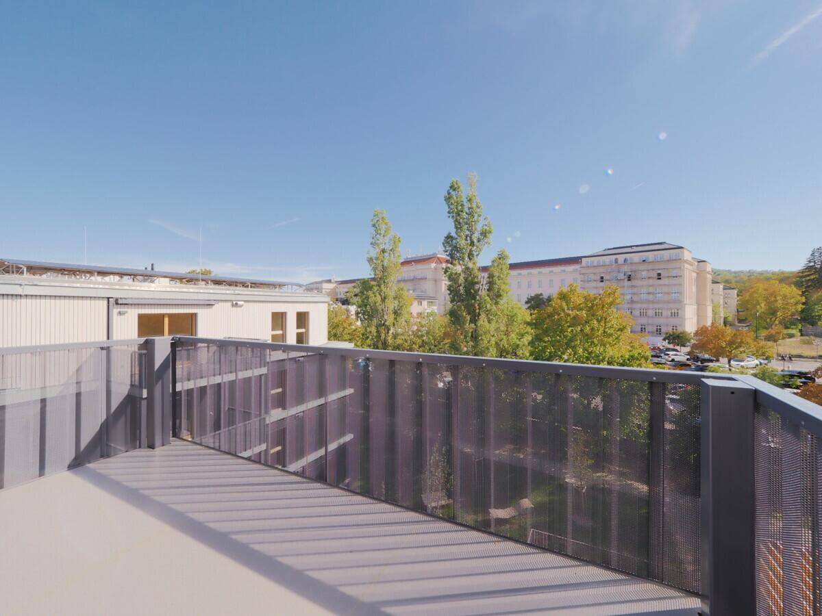 Sonniger Terrassenbereich mit modernem Gittergeländer und Blick auf die umliegenden Gebäude.