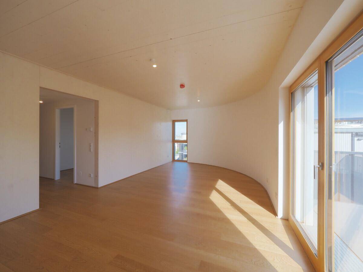 Lichtdurchfluteter Wohnbereich mit Parkettboden, geschwungener Wand und Zugang zu Außenbereichen.
